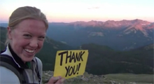 A young lady holding a thank you sign in the wilderness.  Stories about people who have helped others, people who have made a difference because of a service they provided, people who wouldn't be around if they didn't have the CPR assistance of another.